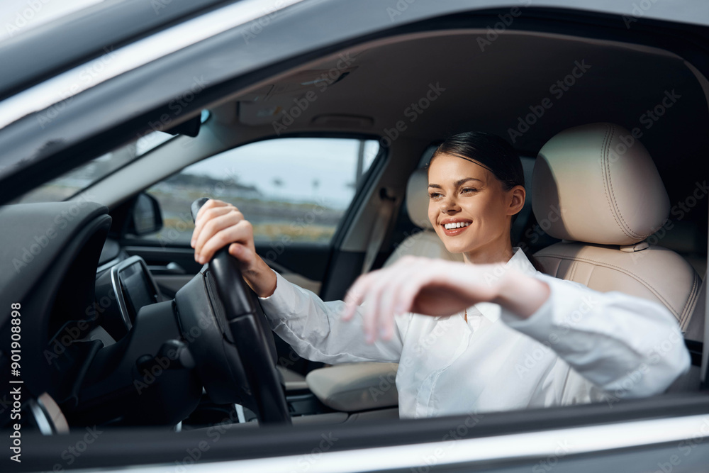 Woman driving a car, hand on the steering wheel, smiling at the camera while seated in the driver's seat Woman driving a car, hand on the steering wheel, smiling at the camera while seated in the driver's seat