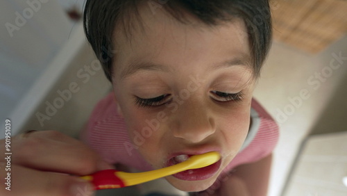 Close-up view of a child brushing teeth, focusing on oral hygiene, with a vibrant toothbrush, emphasizing the importance of dental care in early childhood, taken from an overhead angle