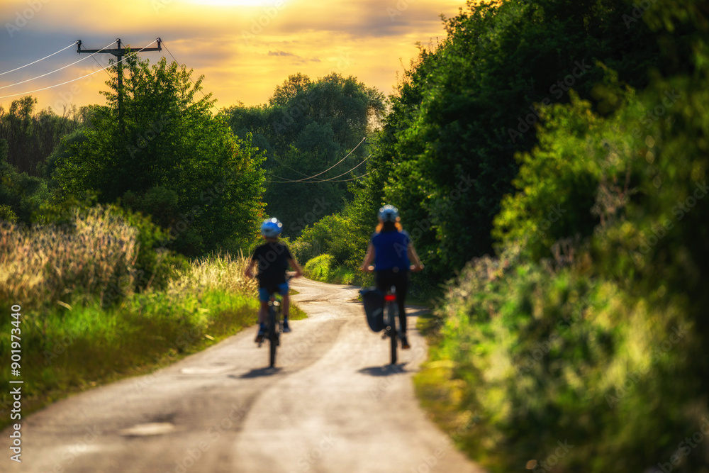 Fototapeta premium Schöner Radweg in der Natur mit zwei Fahrradfahrern bei Sonnenuntergang