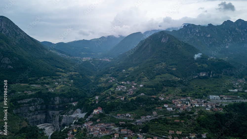 Fototapeta premium Aerial View of Lush Mountains With Small Villages Beneath Overcast Sky in Italy