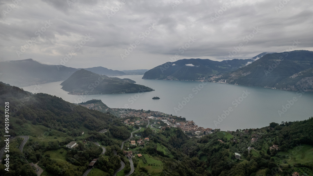Obraz premium Majestic View Over Lake Iseo Surrounded by Rolling Hills Under Cloudy Skies