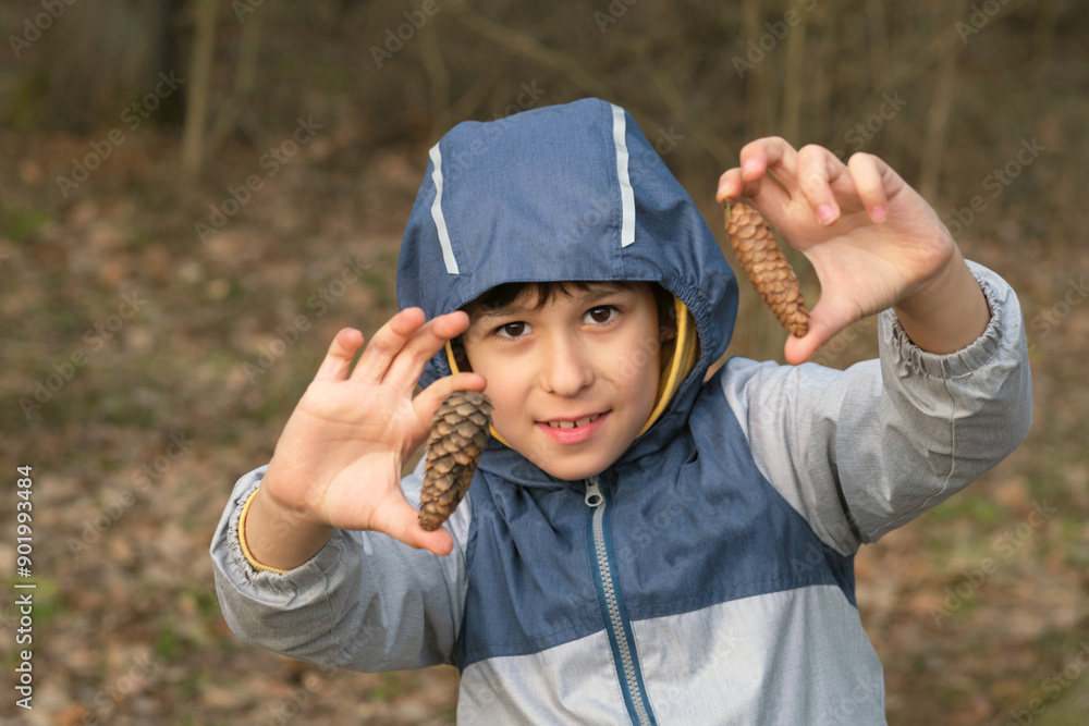 Young boy outdoors in a blue jacket, presenting two pine cones with a cheerful expression. Concept: Demonstrating the benefits of outdoor play and exploration in promoting healthy, active lifestyles Young boy outdoors in a blue jacket, presenting two pine cones with a cheerful expression. Concept: Demonstrating the benefits of outdoor play and exploration in promoting healthy, active lifestyles