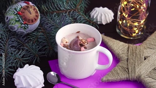 Hot chocolate bomb with marshmallow melts in white cup of hot milk on table at christmas decorations