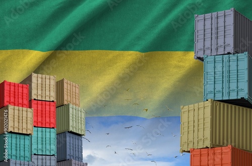 Gabon flag and big stack of shipping cargo containers in docks with sky background close up photo