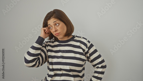 Hispanic middle-aged woman in striped shirt posing with a pensive expression against a white wall.