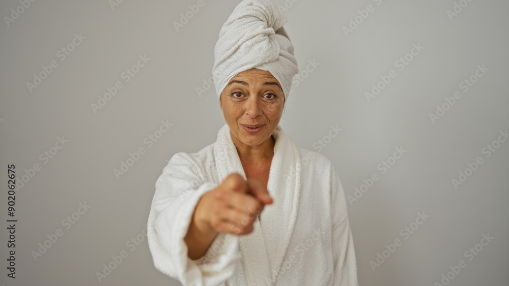 Middle-aged hispanic woman in a white bathrobe and towel turban smiling and pointing at the camera, isolated on a white background Middle-aged hispanic woman in a white bathrobe and towel turban smiling and pointing at the camera, isolated on a white background