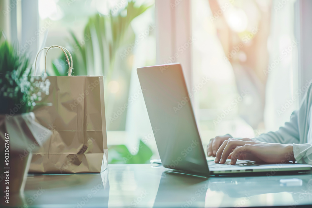 Person working in laptop on a desk, representing online shopping from home with shopping paper bag over the table. Person working in laptop on a desk, representing online shopping from home with shopping paper bag over the table.