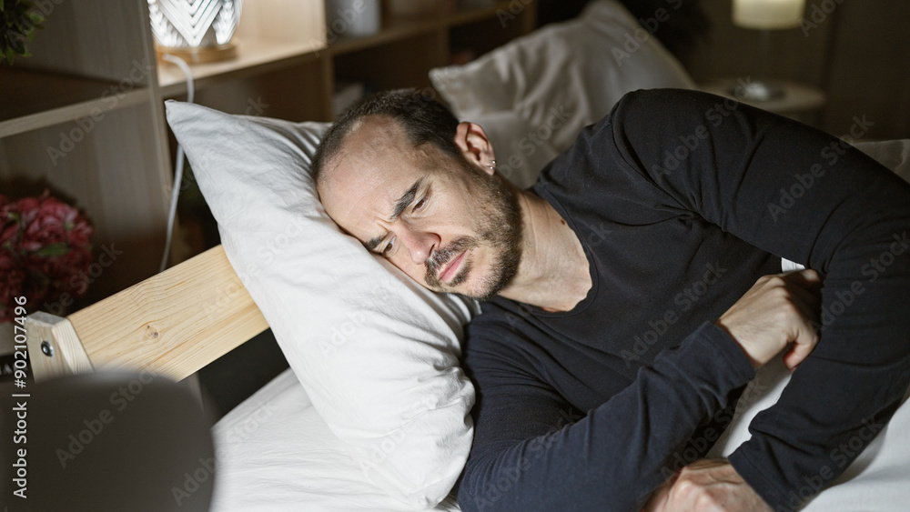 Hispanic bald man with beard sleeps uncomfortably in a dark bedroom, showing insomnia. Hispanic bald man with beard sleeps uncomfortably in a dark bedroom, showing insomnia.