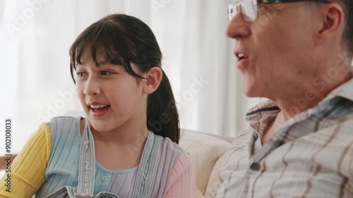 Grandfather and granddaughter together watch interesting entertainment media on TV. Old senior use technology communicate with young generation cross generation gap strengthen family bond. Divergence.