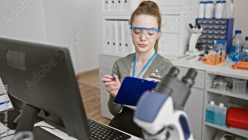 A young caucasian woman in a laboratory analyzing a sample while using a computer indoors