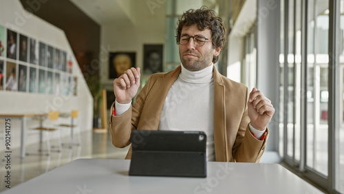 A contented bearded hispanic man in a modern office, listening to music on a tablet with his eyes closed. photo