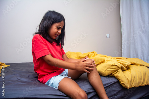 Little girl sitting on her bed holding her knee in pain