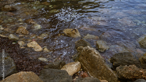 Rocky shore with water gently lapping against various sized rocks and pebbles, creating a serene natural coastal scene. photo