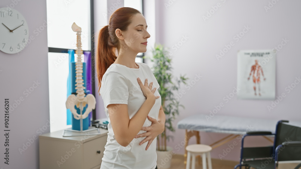 A serene young woman with red hair stands in a light-filled rehab clinic room, a model spine nearby. A serene young woman with red hair stands in a light-filled rehab clinic room, a model spine nearby.