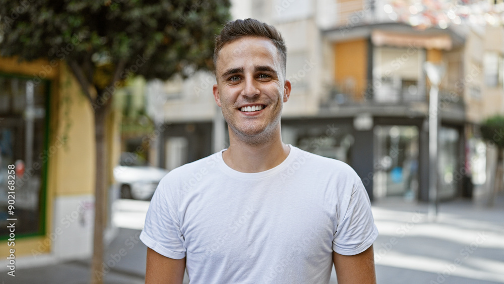 A handsome young hispanic man smiling confidently outdoors on a sunny urban street.