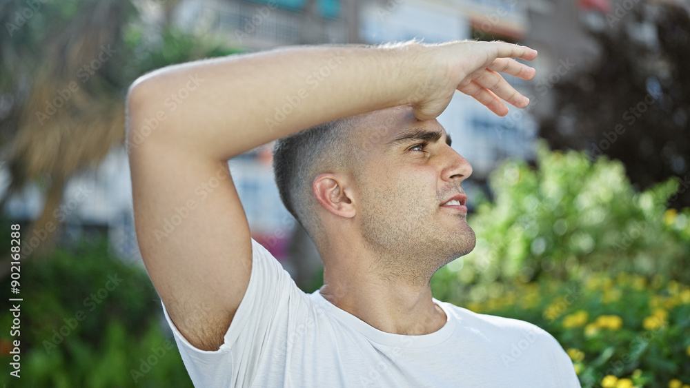Obraz premium A young hispanic man shields his eyes from the sun in an urban park.