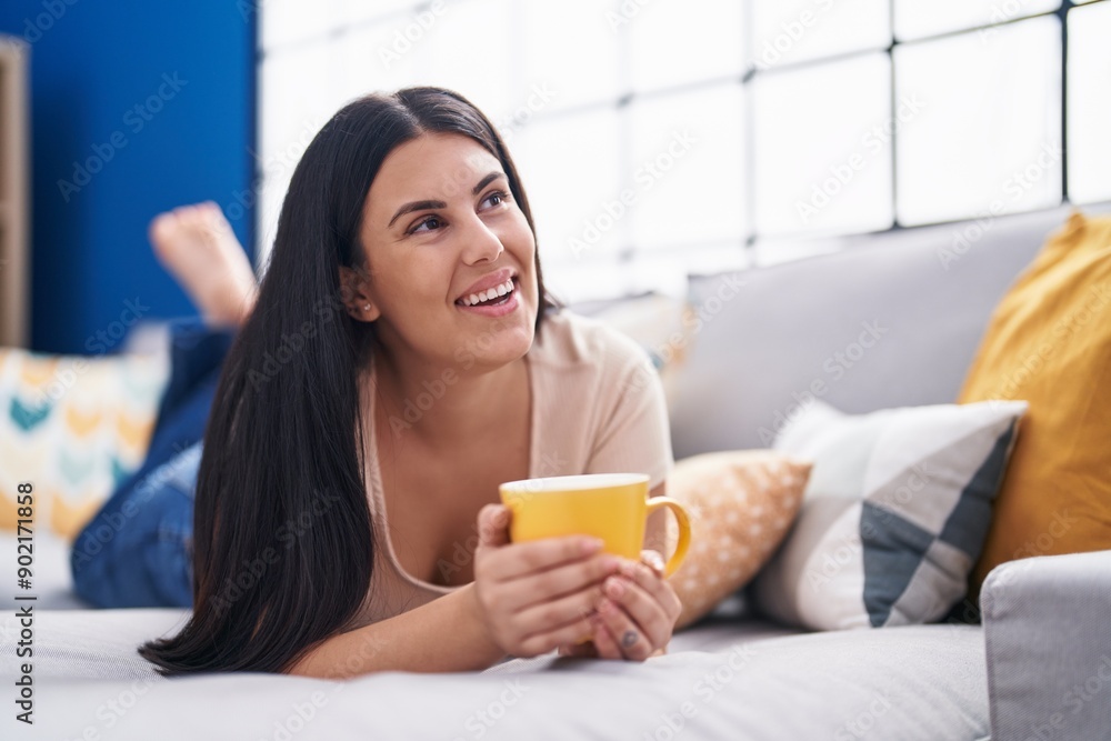 Young beautiful hispanic woman drinking coffee lying on sofa at home Young beautiful hispanic woman drinking coffee lying on sofa at home