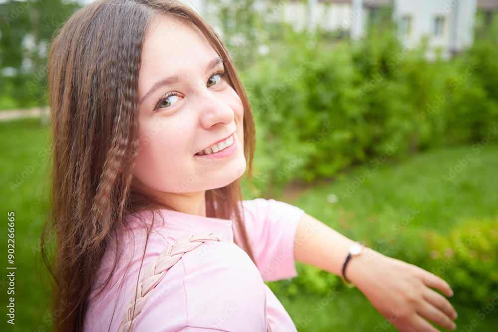 A woman with long brown hair smiles as she checks the time on her wristwatch, standing outside with greenery in the background A woman with long brown hair smiles as she checks the time on her wristwatch, standing outside with greenery in the background