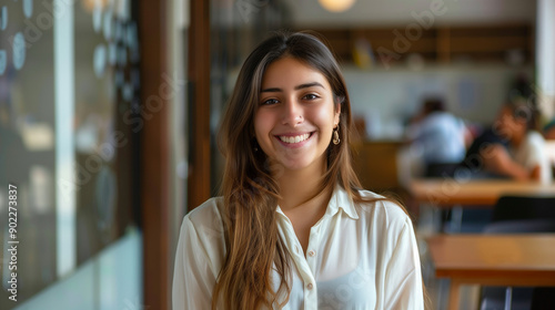 Young smiling latin girl college student or teacher looking at camera standing in university campus. Happy hispanic millennial woman professional posing in modern coworking creative office space