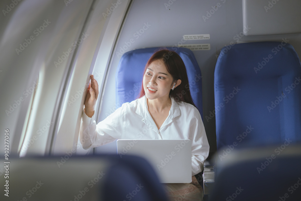 A beautiful woman enjoys her airplane journey, sitting comfortably and smiling. Captured in vibrant photography, she epitomizes excitement and happiness, using wireless technology to stay connected du A beautiful woman enjoys her airplane journey, sitting comfortably and smiling. Captured in vibrant photography, she epitomizes excitement and happiness, using wireless technology to stay connected du