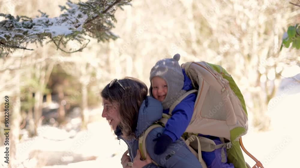 A joyful mother carries her child in a backpack carrier while hiking through a snowy forest. Perfect for family, adventure, and winter activity themes. High quality 4k footage A joyful mother carries her child in a backpack carrier while hiking through a snowy forest. Perfect for family, adventure, and winter activity themes. High quality 4k footage