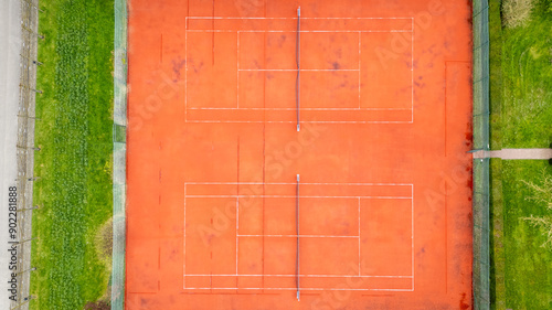 A highangle shot captures clay tennis courts with their distinct lines and net structures, set amidst lush greenery photo