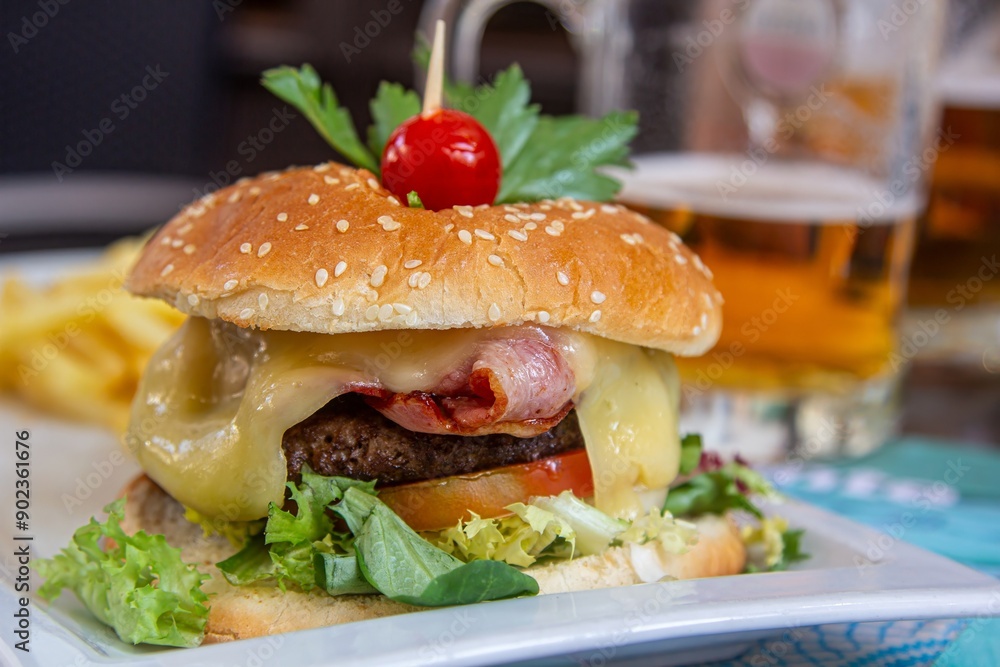 Jugosa hamburguesa con queso, tocino, vegetales y papas fritas con una cerveza de fondo. Jugosa hamburguesa con queso, tocino, vegetales y papas fritas con una cerveza de fondo.