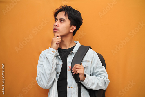 Foto portrait of asian student carrying backpack with his hand on his chin in attenti