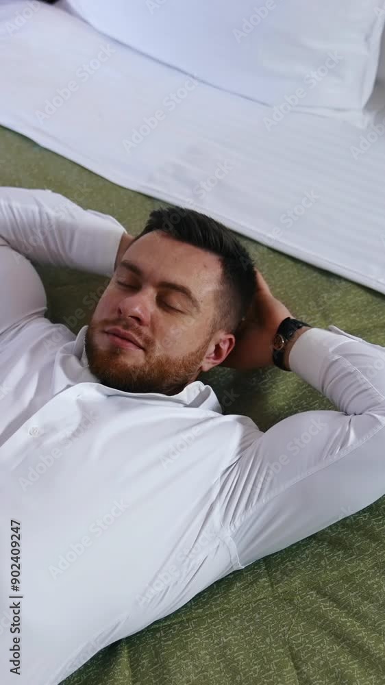 Young businessman relaxing on bed. Handsome man in white shirt is lying on bed enjoying rest alone in a hotel room. Vacation during business trip. Vertical video Young businessman relaxing on bed. Handsome man in white shirt is lying on bed enjoying rest alone in a hotel room. Vacation during business trip. Vertical video
