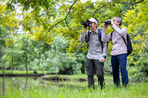 Asian senior man and his son are trekking in the forest while taking photo of wildlife for weekend vacation adventure and family outdoor activities photo