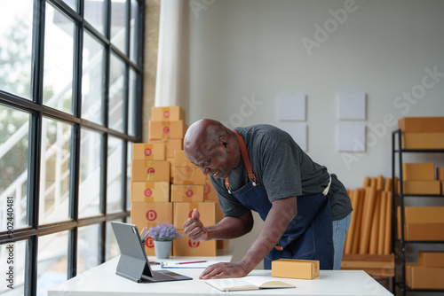 Small Business Startup, SME Owner, American Male Entrepreneur African receives money, expresses joy successful Check online orders to prepare to pack products into boxes and ship them online. photo