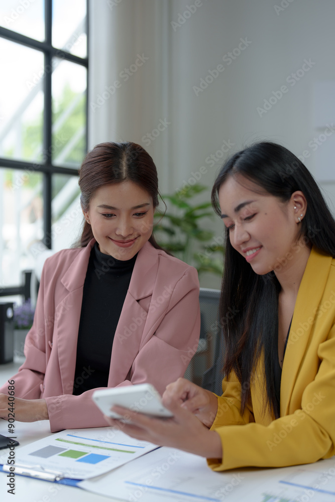 Two confident Asian businesswomen sitting at a table with laptops doing documents together and discussing reports. Project financial calculations brainstorming ideas. Two confident Asian businesswomen sitting at a table with laptops doing documents together and discussing reports. Project financial calculations brainstorming ideas.