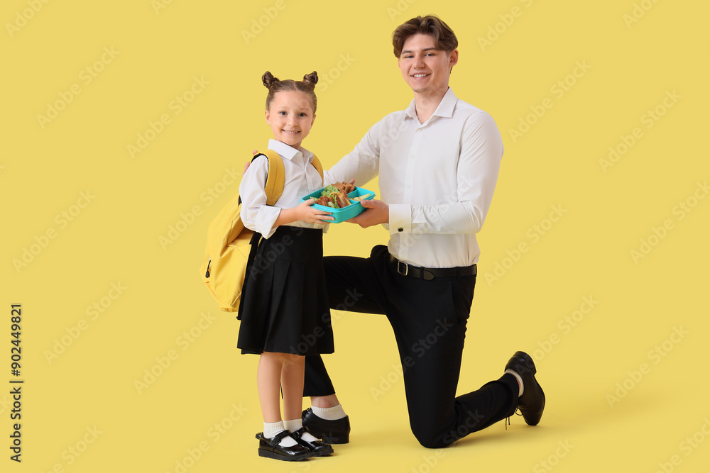 Fototapeta premium Little girl with school lunchbox and her father on yellow background