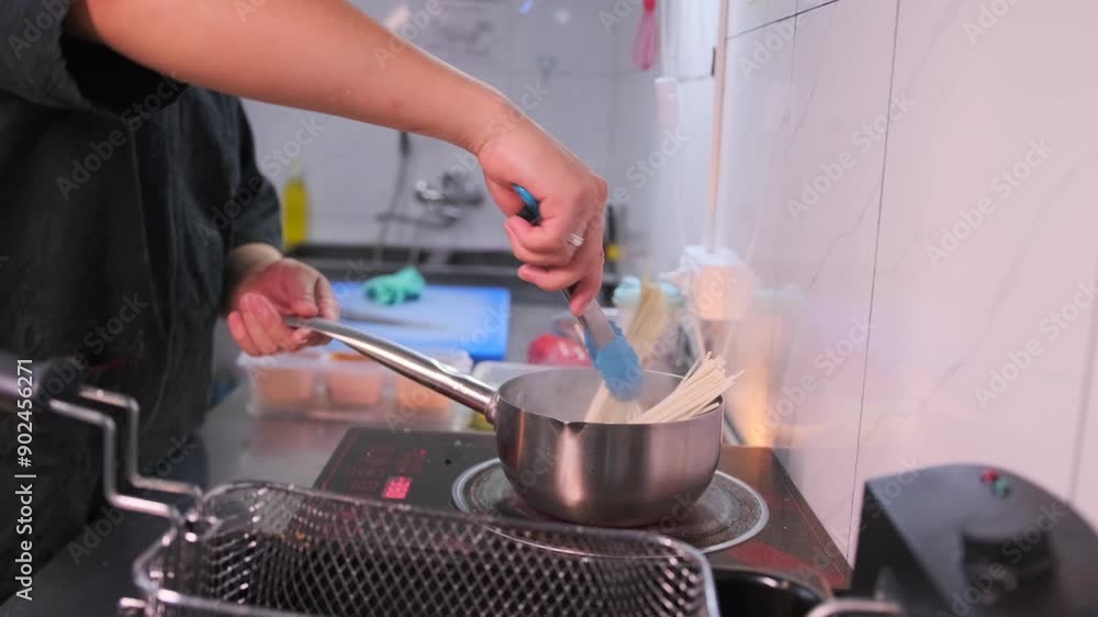 Cooking white soba pasta with stirring the noodles with special tongs in a steel pan on the stove in the kitchen restaurant, close-up. Cooking white soba pasta with stirring the noodles with special tongs in a steel pan on the stove in the kitchen restaurant, close-up.