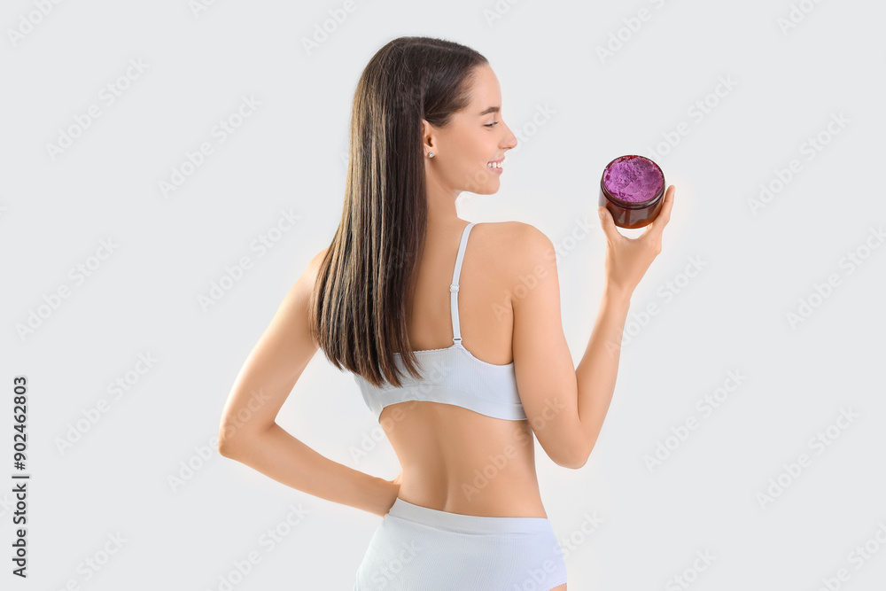 Beautiful young happy woman with jar of body scrub on grey background Beautiful young happy woman with jar of body scrub on grey background