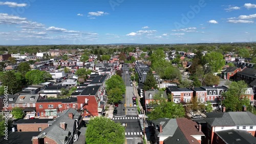 Charming american neighborhood with main street during sunny day with blue sky. Historic Buildings and homes with green trees in spring. Rising drone wide shot. photo