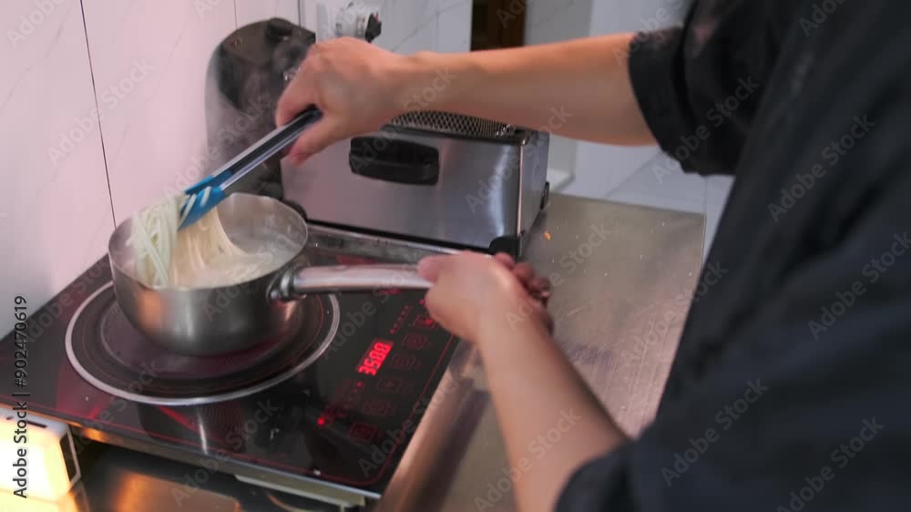 Asian chef cooks white soba noodles in boiling water stirring close up. Slow motion.