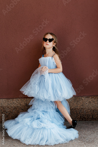 Full length of beautiful little girl in blue poofy dress and sunglasses standing and posing
