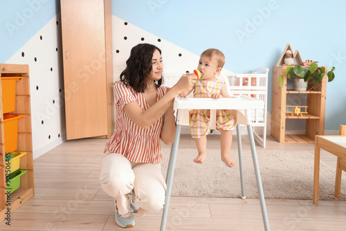 Mother giving her little baby nibbler with food in bedroom