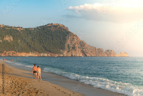 Fototapeta Naklejka Na Ścianę i Meble -  .A couple walk along an empty Cleopatra Beach at sunset in the Turkish holiday resort town of Alanya on the Mediterranean coast of Turkey, the Turkish Riviera. .