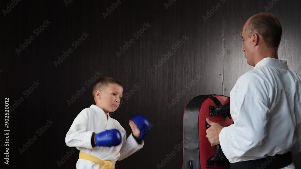 Little athlete with yellow belt trains punches on big exercise machine in motion Little athlete with yellow belt trains punches on big exercise machine in motion