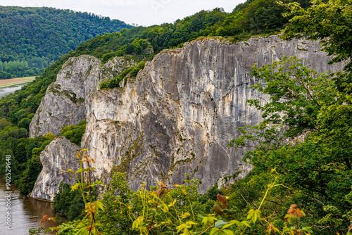 Rock formation known as Freyr Rocks, among hills with green leafed trees, irregular rock wall, next to Meuse river, famous climbing place, cloudy summer day in province of Namur, Wallonia, Belgium