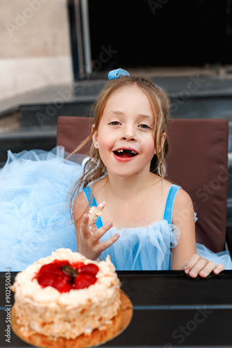 Funny excited toothless girl 5 or 6 years old with Birthday cake sitting in street cafe. Kid birthday