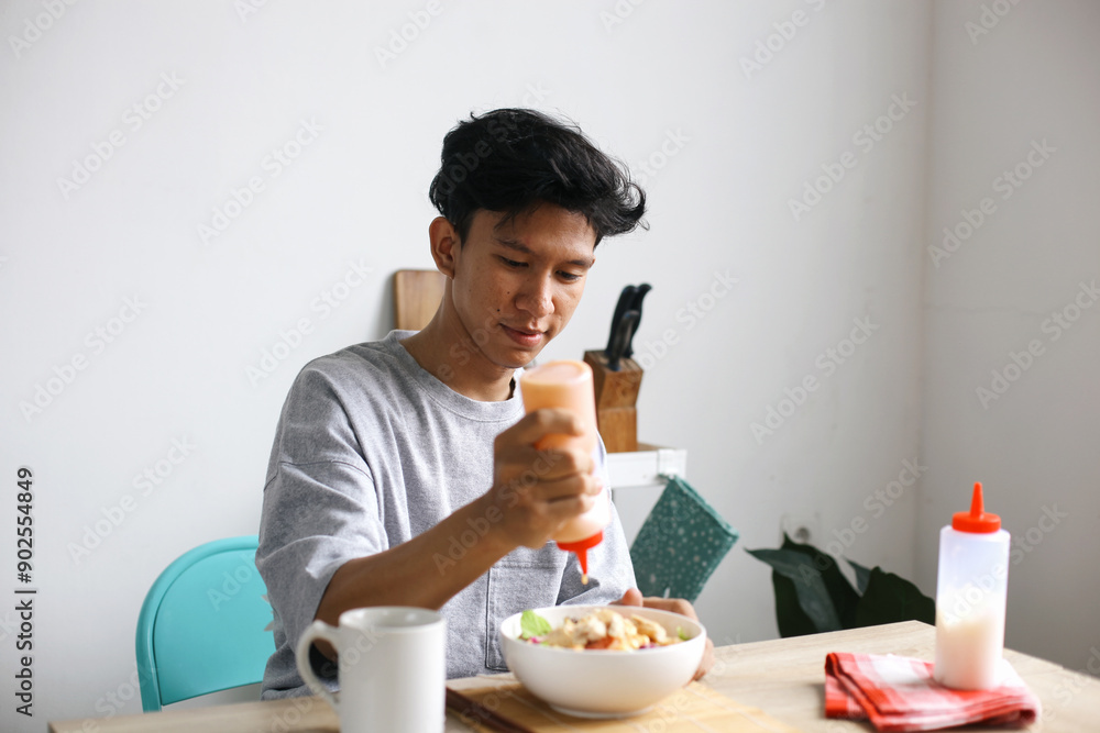 Young Man Pouring Dressing On Fresh Salad At Table Young Man Pouring Dressing On Fresh Salad At Table