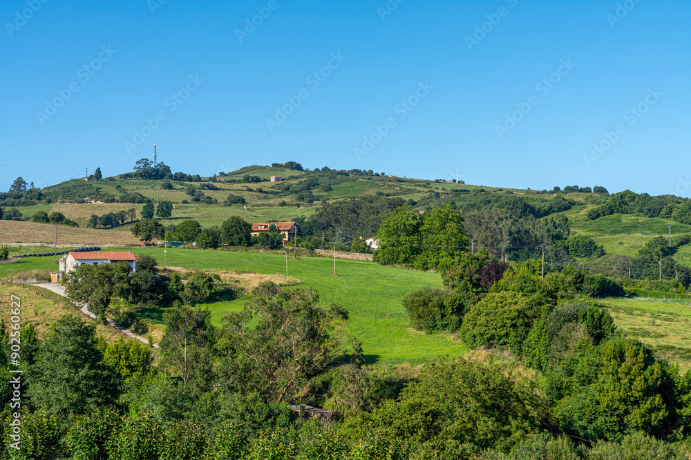 Fototapeta premium Panoramic view of the picturesque town of Santillana del Mar in Cantabria, Spain. The landscape features traditional stone buildings, lush green fields, and a clear blue sky.