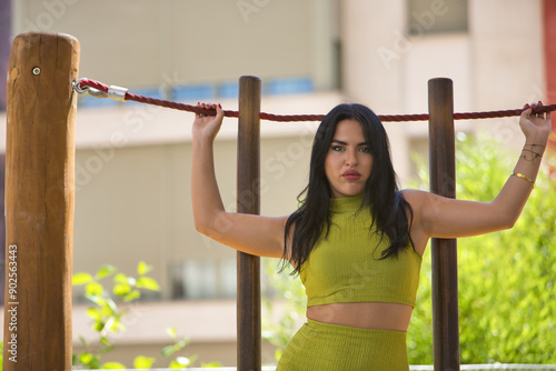 Young, beautiful, brunette, latina woman, wearing a green suit, with a sensual and provocative look while holding a rope with her hands. Concept beauty, fashion, trend, city. photo