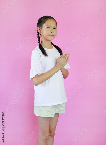 Pretty Asian young girl ages 9 years old Pay respect or pray posture isolated on pink studio background. Side view. photo