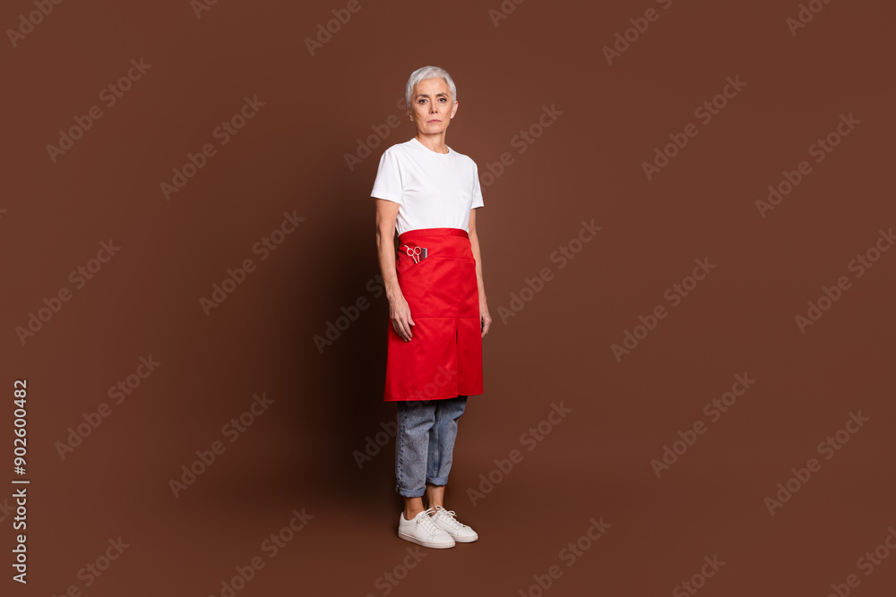 Full size photo of pretty senior female professional hairdresser beauty salon owner wear uniform isolated on brown color background Full size photo of pretty senior female professional hairdresser beauty salon owner wear uniform isolated on brown color background