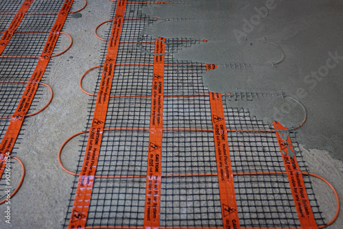 Underfloor heating installation. Electric cabling and conductive meshwork is seen. The pouring of concrete over the top has already begun.