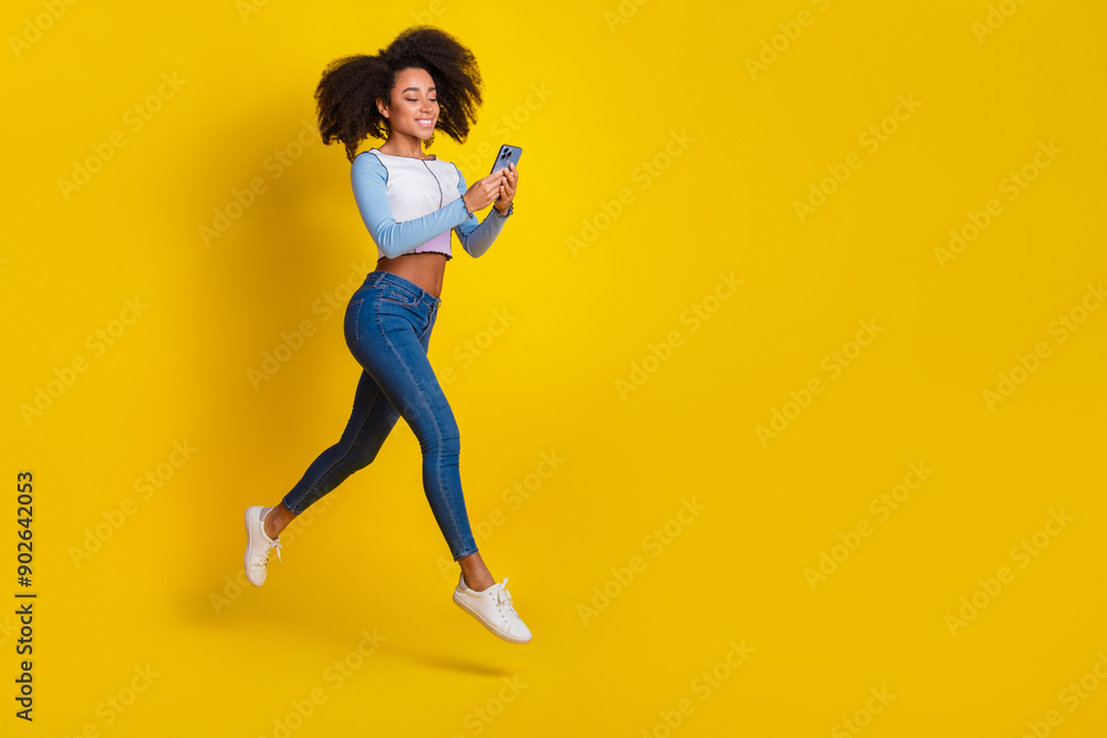 Full size photo of pretty young girl running hold gadget wear trendy blue outfit isolated on yellow color background